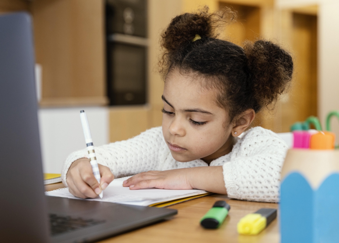 Girl writing on a pad in front of a monitor